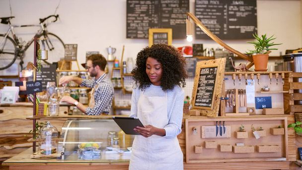 Usmívající se mladá Afroameričanka barista pomocí digitálního tabletu, zatímco stojí před pultem módní kavárny  - Fotografie, Obrázek