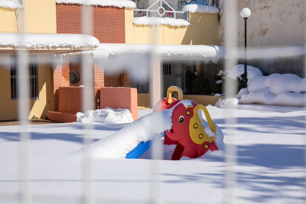 Yunanistan 'ın başkenti Atina' da renkli bir kaydırak ile bir anaokulunun boş oyun bahçesini kış sabahı karları kapladı. - Fotoğraf, Görsel