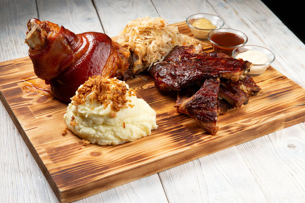 Traditional German beer snacks. Shank, stewed cabbage, fried ribs, mashed potatoes. On a wood panel - Photo, Image