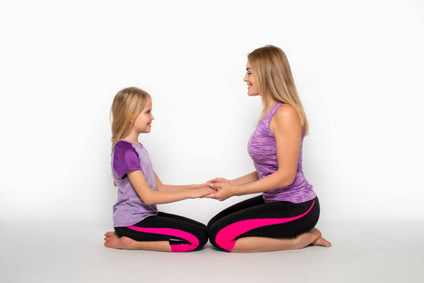 Studio shot di mamma e figlia che indossano tute da ginnastica sul pavimento tenendosi per mano con amore  - Foto, immagini
