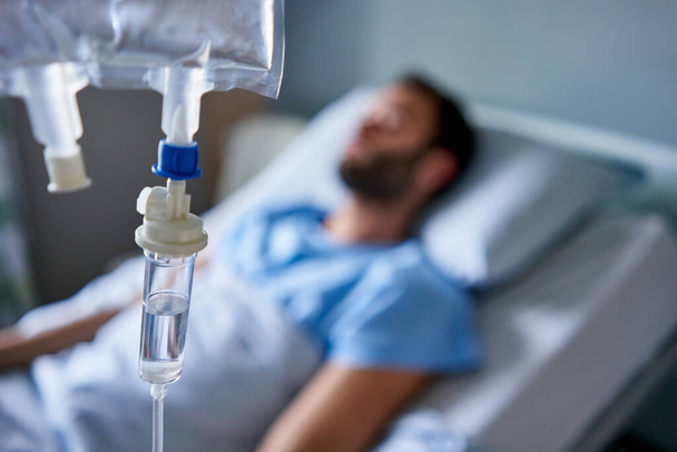 病院のベッドに横たわっ病気の男を治療するために使用されている静脈点滴治療  - 写真・画像