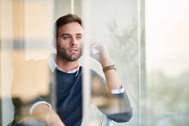 Сосредоточил молодого бизнесмена на разговоре с клиентом по мобильному телефону, выглядывая в окно своего офиса - Фото, изображение