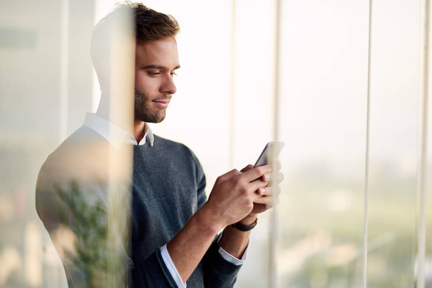 Сосредоточил молодого бизнесмена, стоящего в своем офисе и отправляющего смс-ку на свой мобильный телефон   - Фото, изображение
