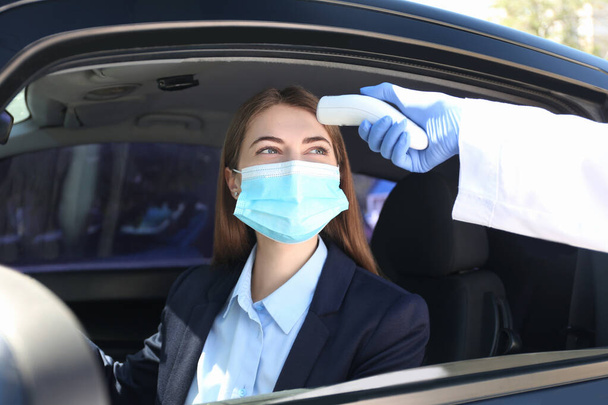 Doctor measuring woman's temperature with non contact infrared thermometer in car - Foto, Imagem