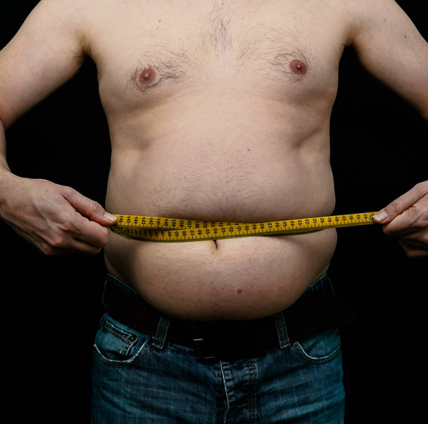 Homem com excesso de peso a medir a barriga. Isolado em fundo preto. Foto de alta qualidade - Foto, Imagem