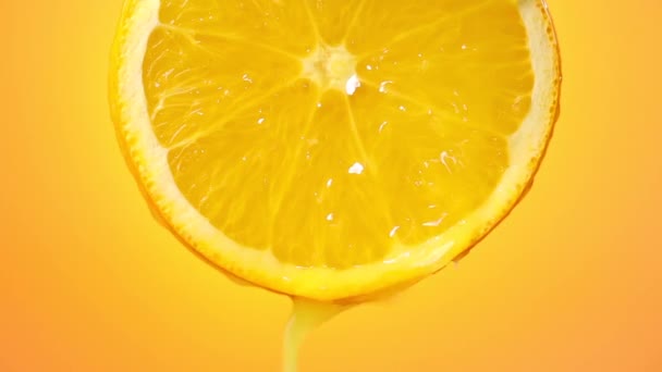 świeżo wyciskany sok pomarańczowy wypływa z dojrzałego plastra owocu blisko - w górę na pomarańczowym tle - Materiał filmowy, wideo