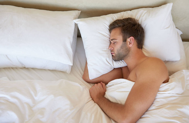 Високий кут пострілу молодого чоловіка зі стерні, мирно спить на м'якій подушці з білим полотном
  - Фото, зображення