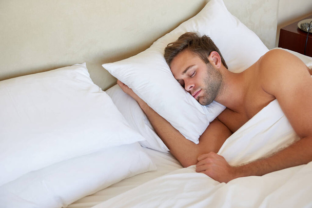 Przystojny młody człowiek śpi głęboko na wygodnej poduszce w podwójnym łóżku z czystą pościelą i miękkimi poduszkami - Zdjęcie, obraz