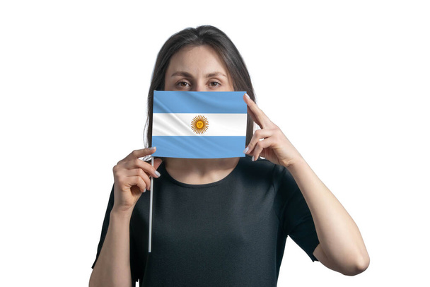 幸せな若い白人女性保持フラグアルゼンチンフラグとそれで彼女の顔をカバー白の背景に隔離. - 写真・画像