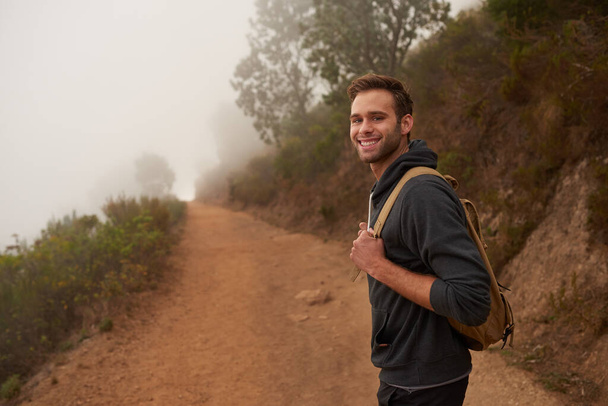Genç bir erkek yürüyüşçü, sisli bir sabahta doğa yürüyüşü yaparken kameraya bakıp gülümsüyor. - Fotoğraf, Görsel