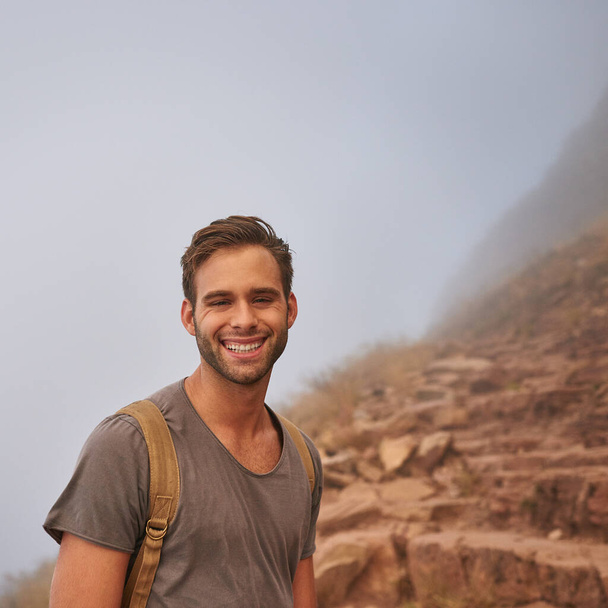 Retrato de un joven excursionista feliz haciendo una pausa en un paseo por la montaña en un sendero rocoso - Foto, Imagen