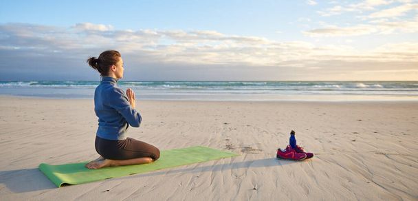 Foto completa de una joven arrodillada meditando en la playa temprano en la mañana  - Foto, imagen