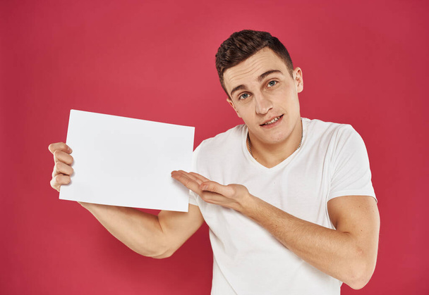 A man with a flyer in his hands on a red background in a white t-shirt cropped view - Foto, Imagen