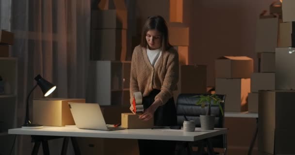 vrouwelijke ondernemer werkt in haar huis magazijn 's nachts, verpakking doos met goederen voor levering in donkere kamer - Video