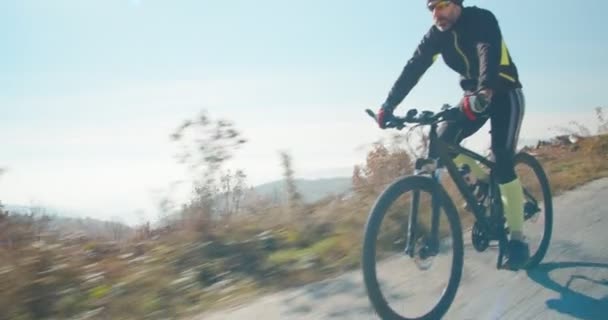 Ποδηλάτης πλήρους απασχόλησης που οδηγεί το ποδήλατό του σε ένα δρόμο στους λόφους του βουνού - Πλάνα, βίντεο