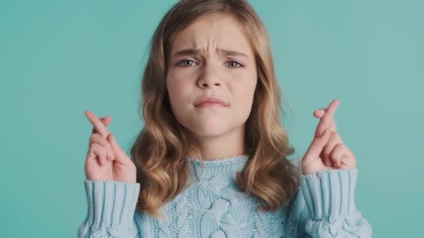 Ανήσυχο ξανθό κορίτσι έφηβος κρατώντας τα δάχτυλα σταυρωμένα ελπίδα να πάρει καλούς βαθμούς στο σχολείο πάνω από πολύχρωμο φόντο. Εκδήλωση προσευχής - Πλάνα, βίντεο