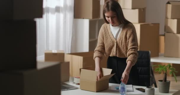 vrouwelijke werknemer zet handgemaakte cosmetica op doos voor de klant, de voorbereiding van goederen voor levering in huis magazijn, eigenaar van kleine bedrijven - Video