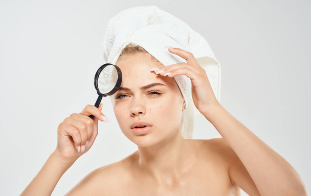 Vrouw met handdoek op het hoofd vergrootglas in de hand naakte schouders kosmetologie dermatologie - Foto, afbeelding