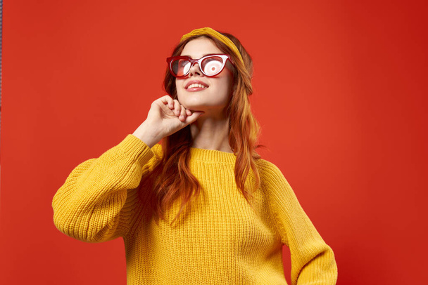 bonita mujer en suéter amarillo gafas rojas ropa de moda primer plano fondo rojo - Foto, imagen