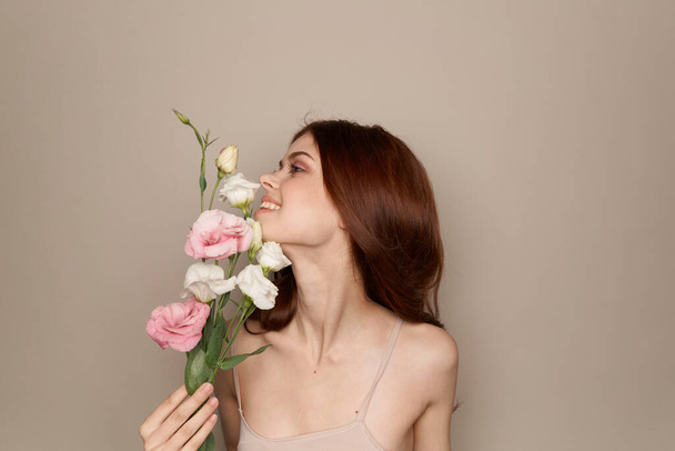 Femme heureuse avec un bouquet de fleurs claires sur un fond beige épaules nues modèle cheveux rouges beau visage - Photo, image