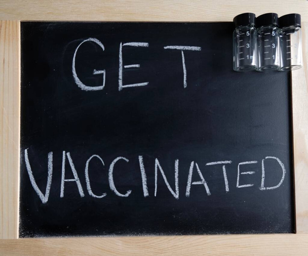 vacunarse por escrito en la pizarra. frascos vacíos junto a signo. - Foto, Imagen
