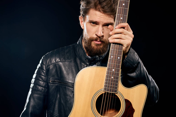 Um homem com uma guitarra em suas mãos jaqueta de couro performance musical rock star estilo moderno fundo escuro - Foto, Imagem