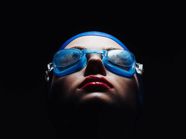 όμορφη γυναίκα σε γυαλιά για κολύμπι και φωτεινό μακιγιάζ κόκκινα χείλη μαύρο φόντο - Φωτογραφία, εικόνα