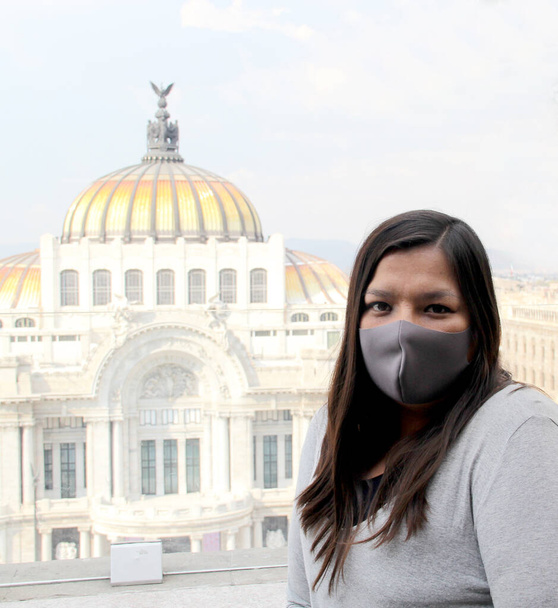 mujer latina con máscara de protección en la ciudad de México con los nuevos monumentos normales e históricos en el fondo, palacio de bellas artes - Foto, Imagen