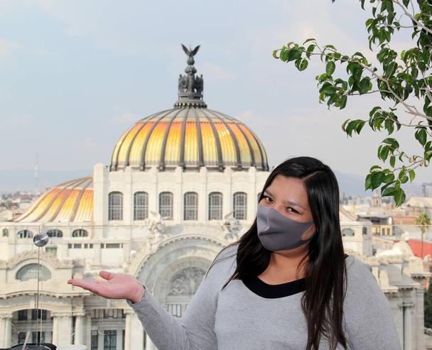 Λατίνα γυναίκα με μάσκα προστασίας στην πόλη του Μεξικού με τα νέα κανονικά και ιστορικά μνημεία στο παρασκήνιο, παλάτι των καλών τεχνών - Φωτογραφία, εικόνα