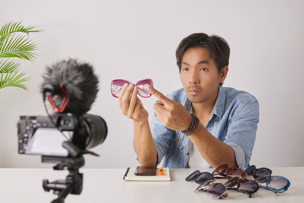Asiatische Vlogger oder Blogger bewerten rosafarbene Modebrillen mit Kunden am Bein und nehmen Videos auf. Freelancer Online-Live-Streaming mit Kunden über Social Media - Foto, Bild