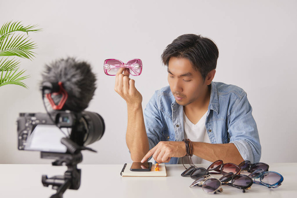 Asiatische Vlogger oder Blogger zeigen rosa Modebrillen und chatten mit Kunden, während sie Videos aufnehmen. Freelancer Online-Live-Streaming mit Kunden über Social Media - Foto, Bild