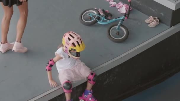 Vista de ángulo alto de la adolescente chica caucásica que usa ropa casual, casco de seguridad y almohadillas que comienzan a patinar en el centro de patinaje interior - Imágenes, Vídeo