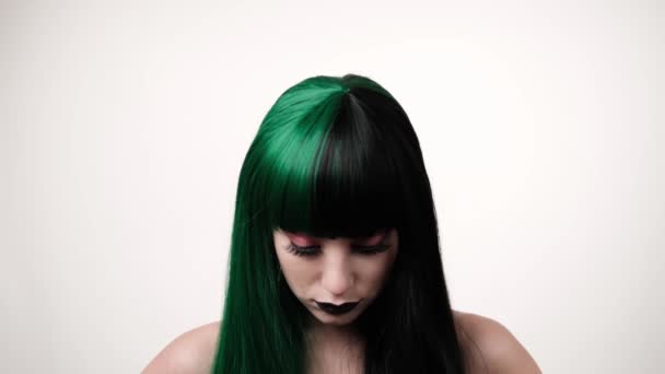 Ritratto di donna caucasica gioiosa elegante in lunga parrucca nero-verde su sfondo lifht. Straordinario fascino femminile. bambola sguardo concetto. - Filmati, video