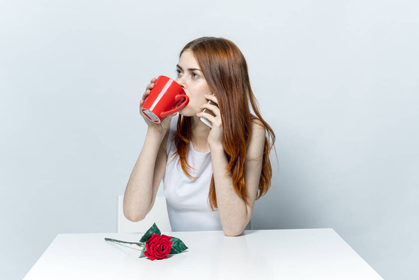 elegant woman sitting at the table drinking from a red mug and talking on the phone - Foto, immagini