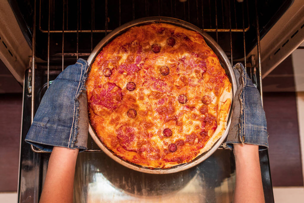 Pohled shora na ženské ruce, jak vytahují připravenou pizzu z trouby. Vařím doma. Nízký DOF. - Fotografie, Obrázek