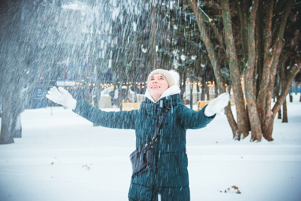 Молода дівчина з блакитними очима кидає пухнастий свіжий сніг на тлі снігопадів і ліхтарів в парку в зимовий день
 - Фото, зображення