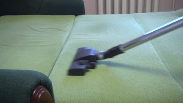 Takarítási szolgáltatás férfi porszívózik a kanapén, porszívó porszívózik zöld ottomán ágy, hétvégi takarítás - Felvétel, videó