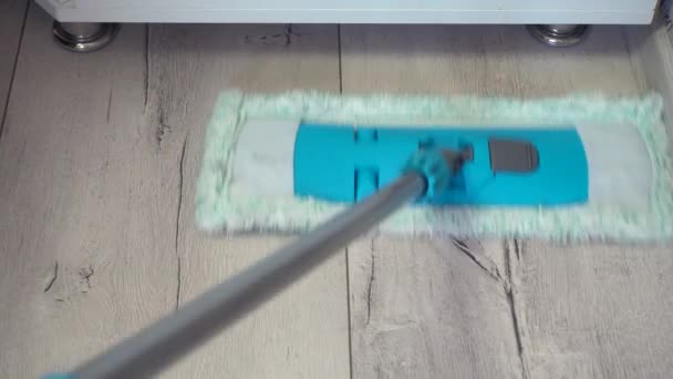 Muž čistí podlahy s mop na šedém laminátovém povrchu v blízkosti podstavce a pod skříní. Detailní záběr - Záběry, video