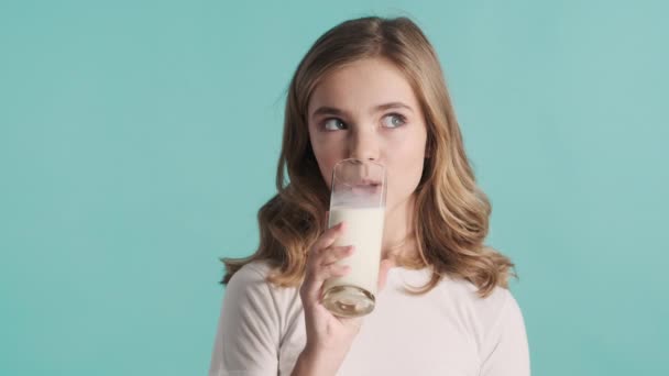Krásná blond dospívající dívka hledá roztomilé pití mléka a usmívá se na kameru přes barevné pozadí. Teen model ve studiu - Záběry, video