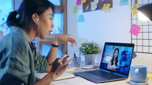 Asia zakenvrouw met behulp van laptop praten met collega 's over het plan in video call vergadering in de woonkamer. Werken vanuit huis overbelasting 's nachts, op afstand werken, sociale afstand, quarantaine voor coronavirus. - Video