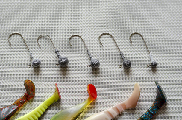 Zufällige Jig Heads und Fragmente von Gummiködern liegen auf einem weiß strukturierten Hintergrund. Ein spezielles Gerät zum Fangen von Raubfischen mit Bleileine und Fischermütze. Verlockungen mit unterschiedlichem Gewicht. - Foto, Bild
