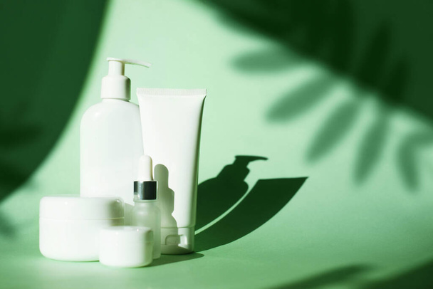 Σετ καλλυντικά μπουκάλι βάζο κρέμα, τζελ, λοσιόν σε πράσινο φόντο με βαθιά φύλλα σκιά. Beauty product mock up package, λευκό πλαστικό δοχείο - Φωτογραφία, εικόνα