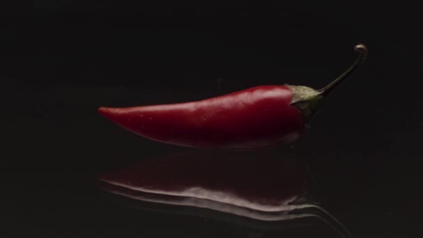 Close up de pimenta vermelha picante deitado na superfície transparente de vidro no fundo preto. Imagens de stock. Legumes frescos, conceito de comida e culinária. - Filmagem, Vídeo