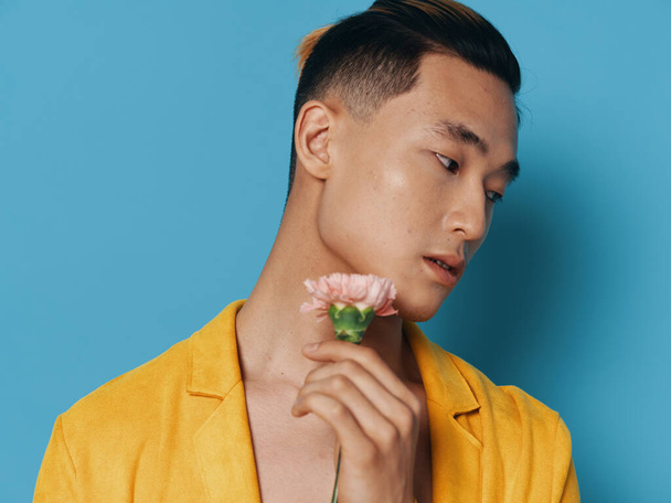 Handsome Asian man with flower romance blue background yellow coat - Фото, зображення