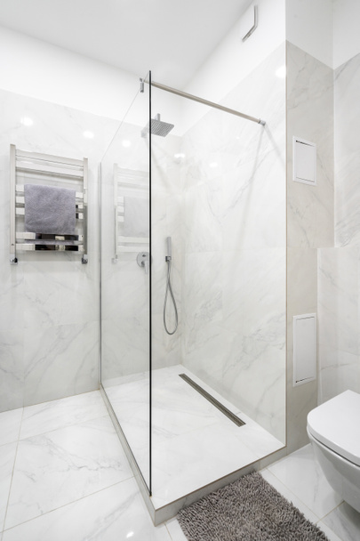 Concept van minimalistisch ruimteontwerp. Verticaal uitzicht op badkamer met modern interieur, sanitair op keramische betegelde muur in douchecabine, handdoek op verwarmde rail en tapijt in de buurt van toilet kom - Foto, afbeelding