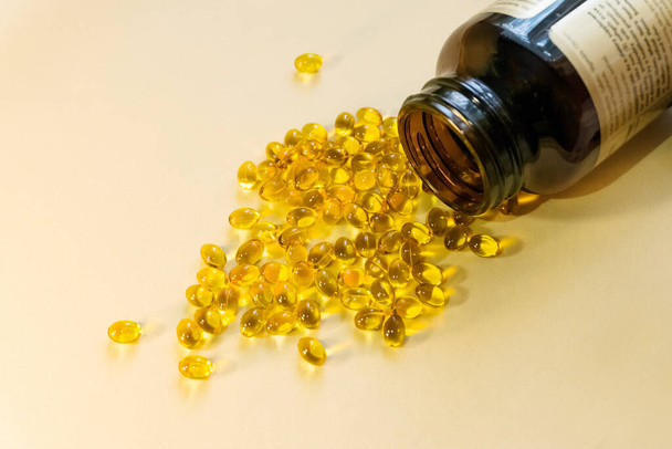 Yellow gel capsules with oil-soluble vitamin are scattered on a light background from a dark glass bottle. Copy space for input the text. - Photo, Image