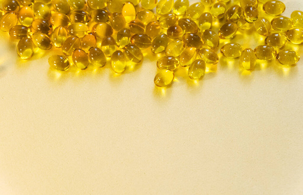 Yellow gel capsules with oil-soluble vitamin are scattered on a light background from a dark glass bottle. Copy space for input the text. - Photo, Image