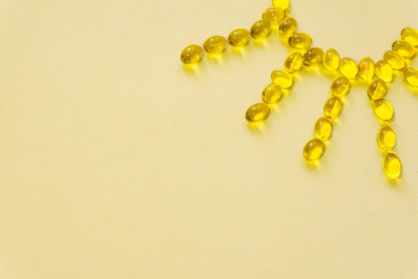 Food supplements. Vitamin D3 capsules shaped in sun symbol on yellow background.Copy space for input the text. - Photo, Image