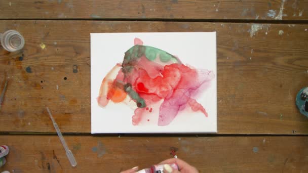 Vista superior da artista feminina pinta um quadro abstrato, ela derrama algumas gotas de dor vermelha para tela molhada e usa secador para distribuí-lo - Filmagem, Vídeo