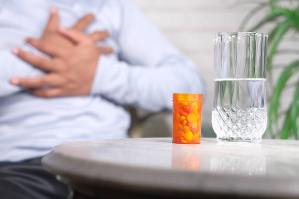pill container on table and a man suffering pain in heart on background  - Photo, Image